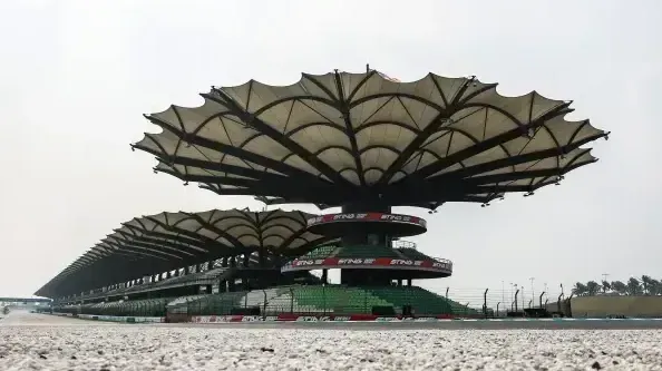 Estrutura de arquibancada com cobertura de guarda-chuva em circuito de Fórmula 1, com pista de asfalto vazia ao fundo sob céu nublado
