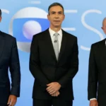 Flávio Bolsonaro, à esquerda, o mediador César Tralli, ao centro, e Lula, à direita, posam lado a lado no cenário do debate da TV Globo, no Rio de Janeiro, em 23 de outubro de 2026