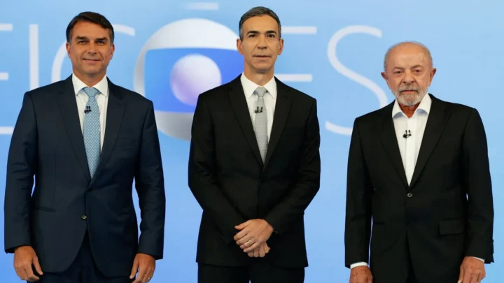 Flávio Bolsonaro, à esquerda, o mediador César Tralli, ao centro, e Lula, à direita, posam lado a lado no cenário do debate da TV Globo, no Rio de Janeiro, em 23 de outubro de 2026