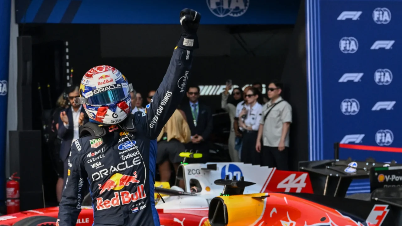 Piloto de Fórmula 1 comemora pole position levantando o punho ao lado de seu carro de corrida, com logotipos da FIA e da categoria visíveis ao fundo