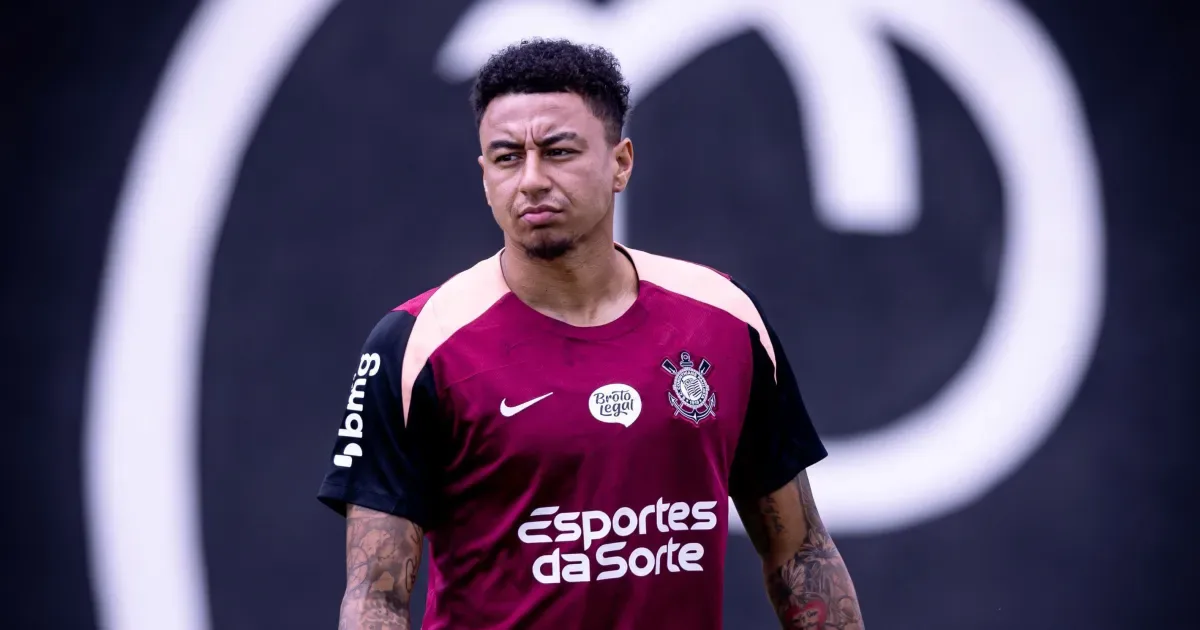 Jogador de camisa vinho do Corinthians, com patrocínios bmg e Esportes da Sorte, em treino no CT, com expressão séria e olhar para o lado