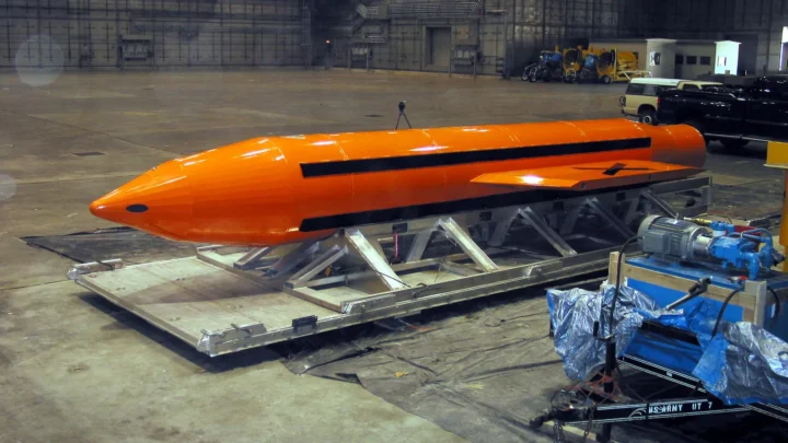 Bomba GBU-43/B, a MOAB, pintada de laranja e apoiada em uma estrutura metálica dentro de um hangar, antes de um teste em 2003