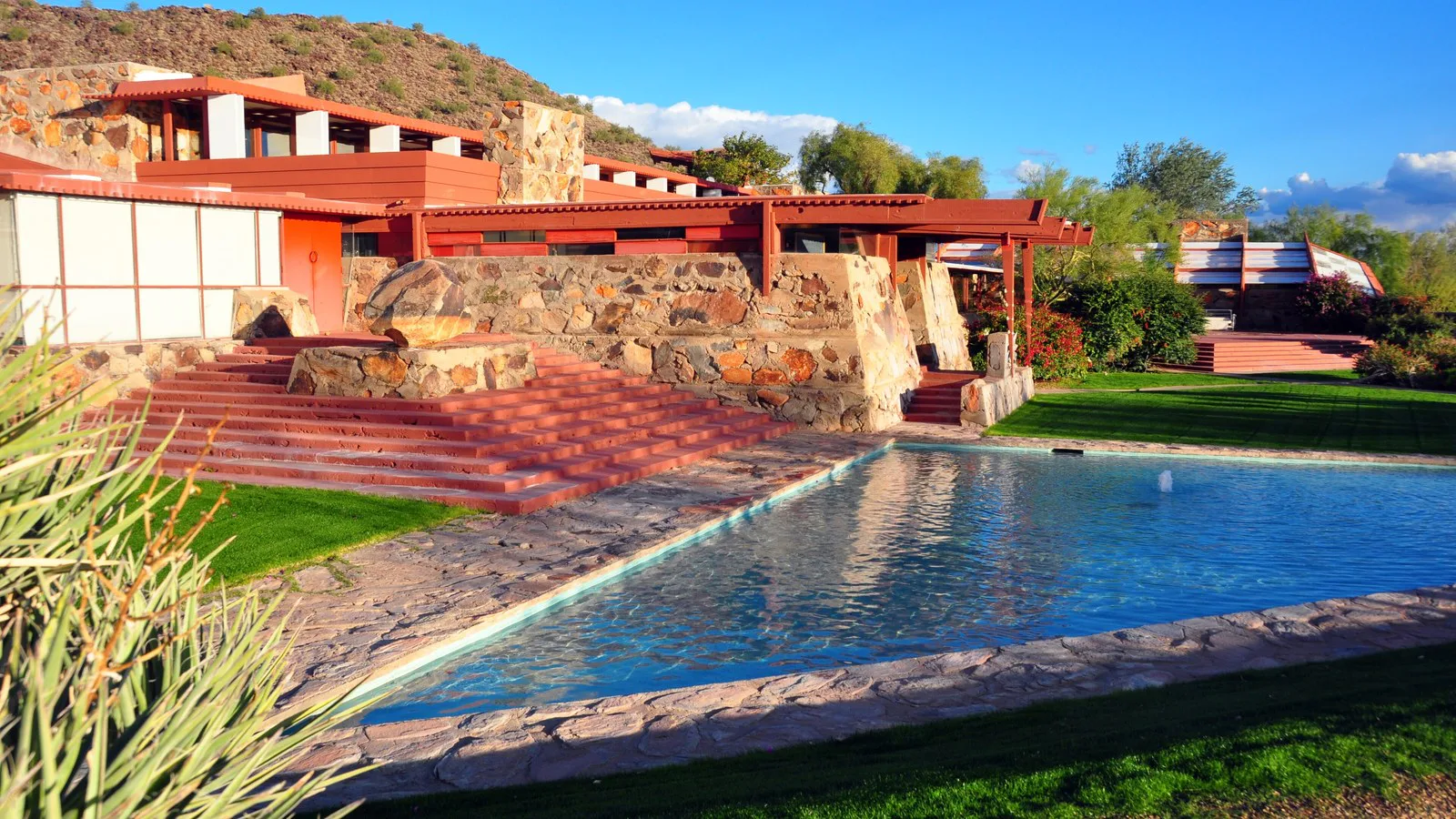 Prédios baixos de pedra e madeira de Taliesin West, com espelho d'água em frente, no deserto de Scottsdale, no Arizona