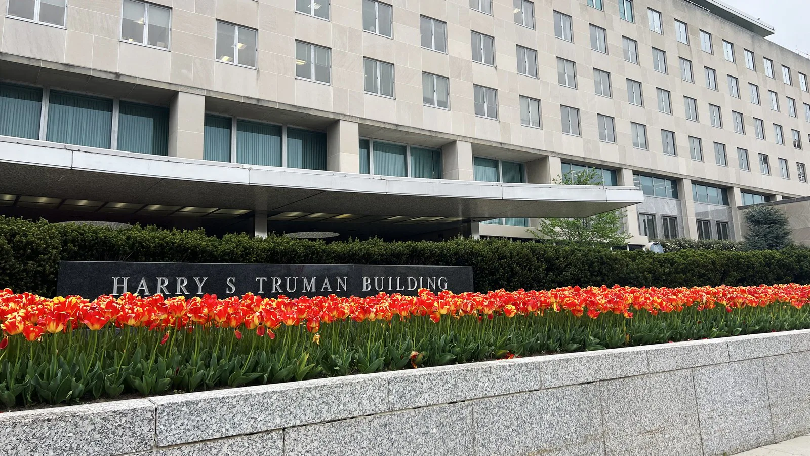 Letreiro Harry S Truman Building com canteiro de tulipas vermelhas e laranja diante da sede do Departamento de Estado, em Washington, em foto de 2024