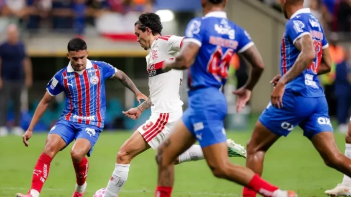Jogador do Flamengo, de branco, conduz a bola cercado por defensores do Bahia, de azul e vermelho, durante partida do Brasileirão