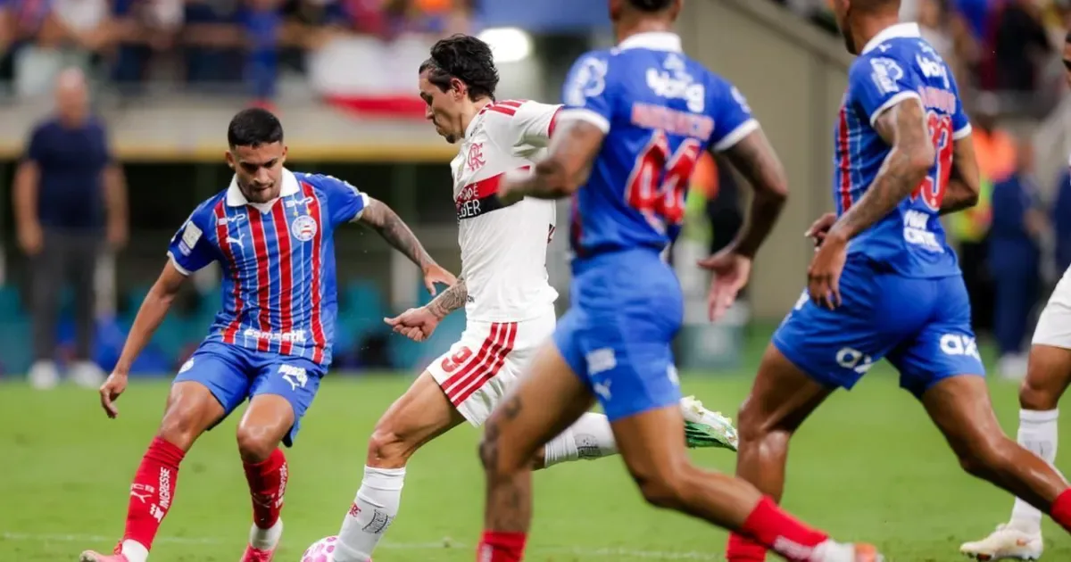 Jogador do Flamengo, de branco, conduz a bola cercado por defensores do Bahia, de azul e vermelho, durante partida do Brasileirão