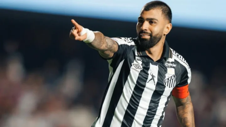 Jogador de uniforme listrado em preto e branco com faixa capitã aponta para o público durante partida