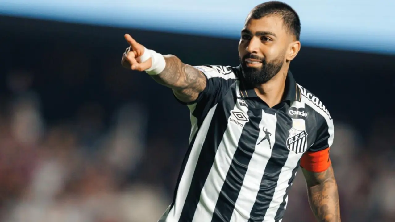 Jogador de uniforme listrado em preto e branco com faixa capitã aponta para o público durante partida