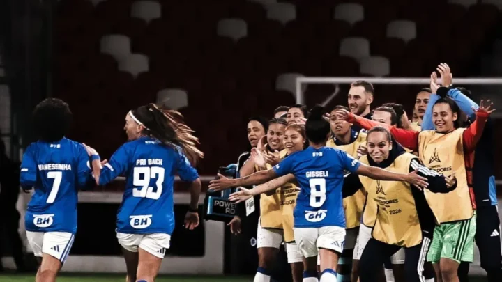Jogadoras do Cruzeiro com camisas azuis e nomes como Vanessinha, Pri Back e Gisselli comemoram em campo, abraçadas a membros da comissão técnica