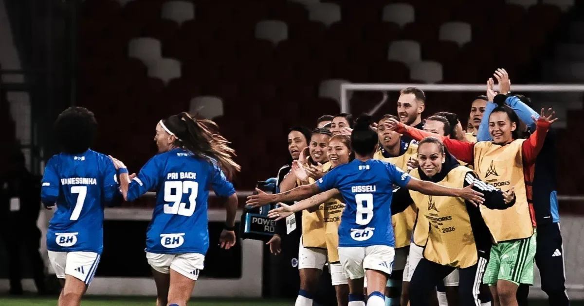 Jogadoras do Cruzeiro com camisas azuis e nomes como Vanessinha, Pri Back e Gisselli comemoram em campo, abraçadas a membros da comissão técnica
