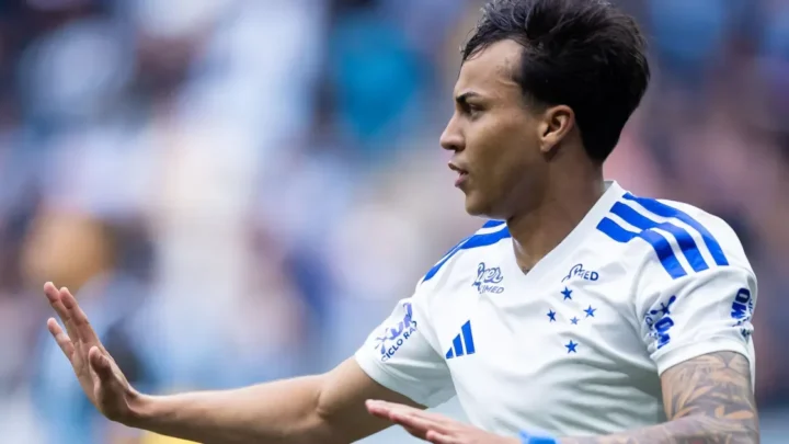 Jogador de camisa branca com detalhes azuis e estrelas do Cruzeiro gesticula com a mão aberta em campo