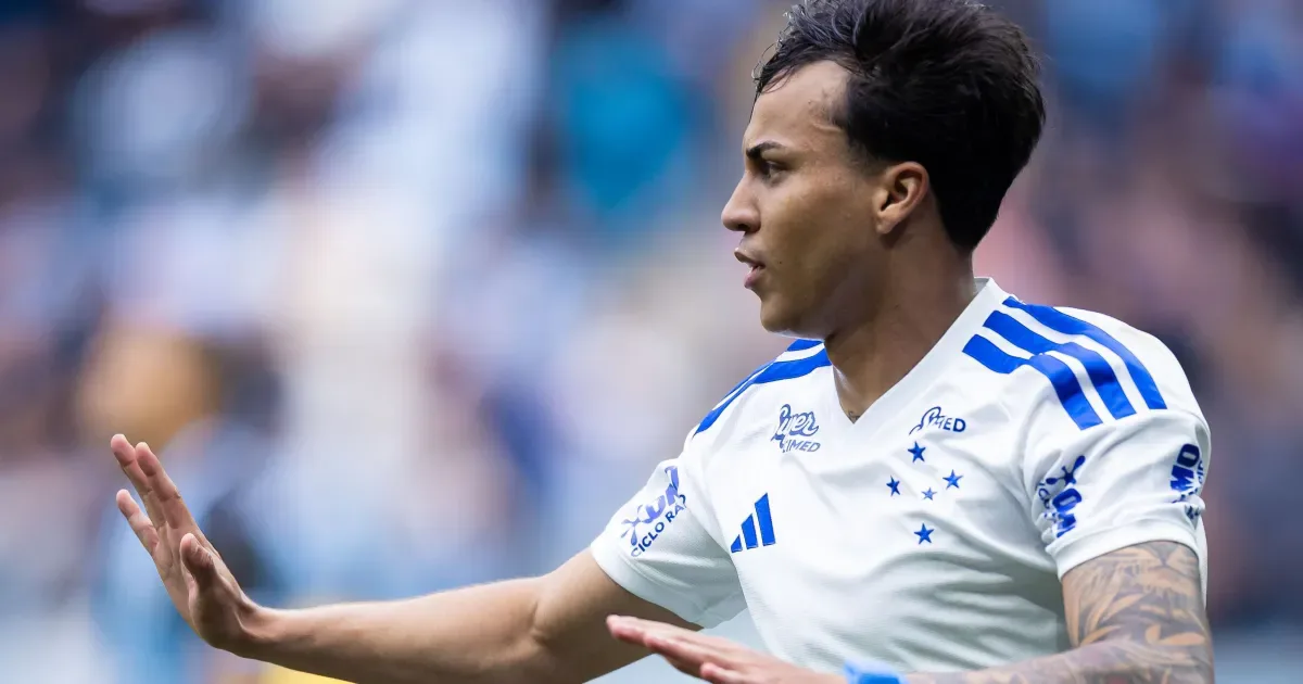 Jogador de camisa branca com detalhes azuis e estrelas do Cruzeiro gesticula com a mão aberta em campo