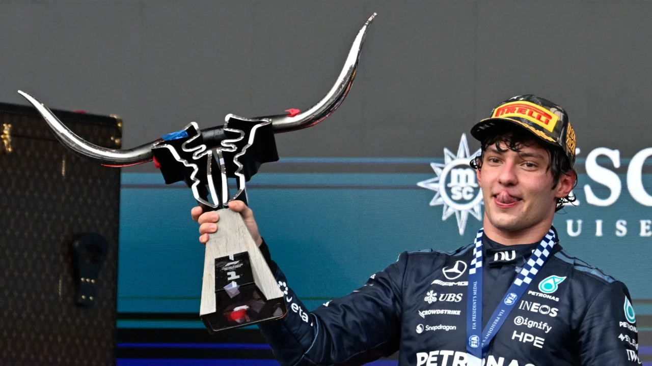 Piloto de macacão preto da Mercedes, com medalha da FIA e boné da Pirelli, ergue troféu em forma de touro durante cerimônia no pódio