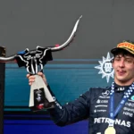 Piloto de macacão preto da Mercedes, com medalha da FIA e boné da Pirelli, ergue troféu em forma de touro durante cerimônia no pódio