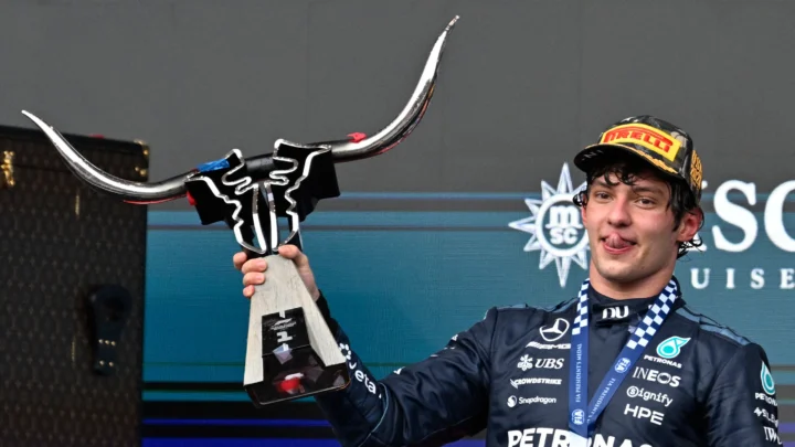 Piloto de macacão preto da Mercedes, com medalha da FIA e boné da Pirelli, ergue troféu em forma de touro durante cerimônia no pódio
