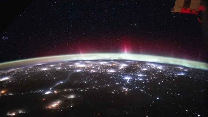 Aurora verde e vermelha sobre a curvatura da Terra, acima das luzes das cidades da Europa e da Rússia, fotografada da Estação Espacial em fevereiro de 2026