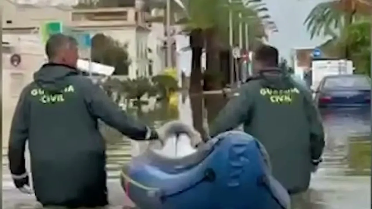 Dois agentes da Guarda Civil, com água acima dos joelhos, puxam um bote inflável por uma rua alagada
