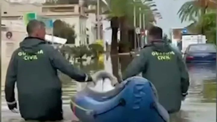 Dois agentes da Guarda Civil, com água acima dos joelhos, puxam um bote inflável por uma rua alagada
