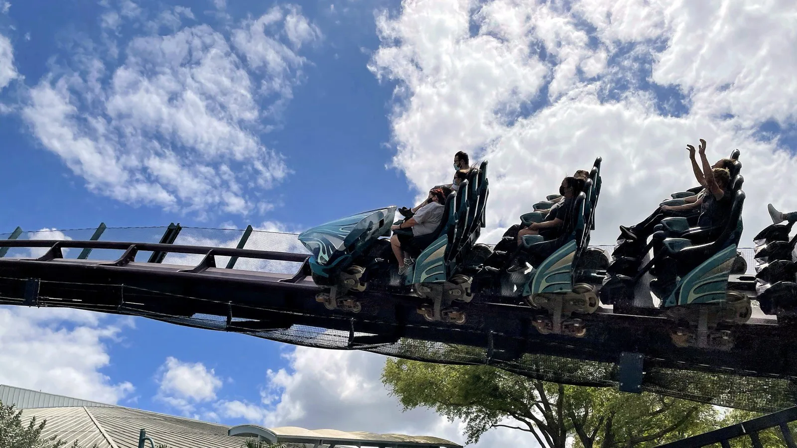 Passageiros com os braços para cima passam em um trem da Mako, com bancos abertos e travas individuais de colo