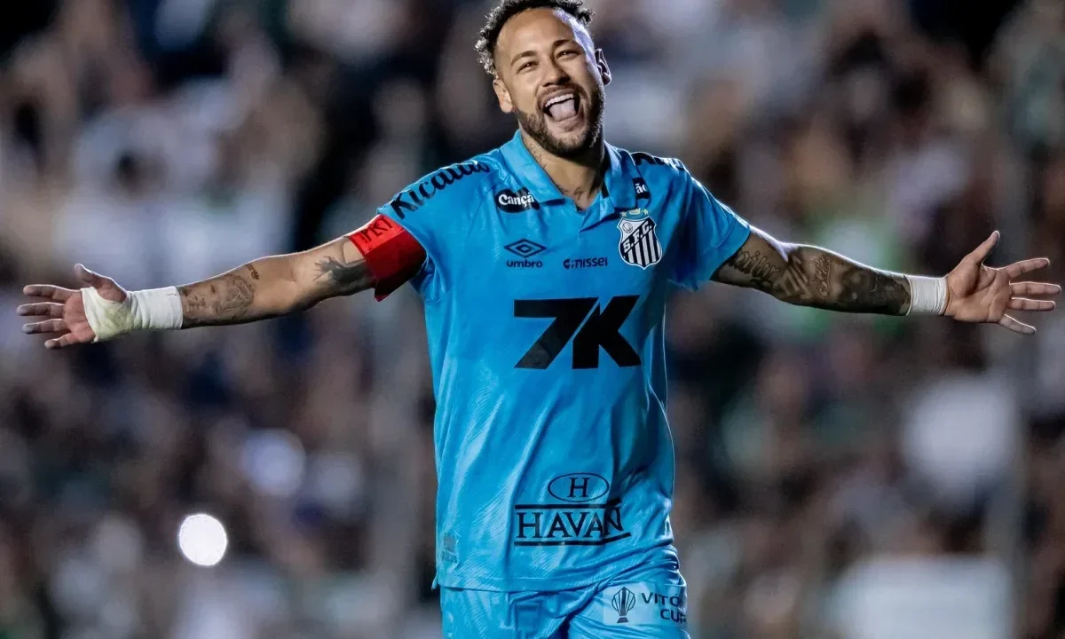 Jogador de camisa azul do Santos, com faixa de capitão no braço, comemora de braços abertos e sorrindo em um estádio