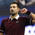 Tenista em quadra durante partida do ATP 500 de Pequim, vestindo polo bordô com detalhes brancos e pulseira de suor roxa