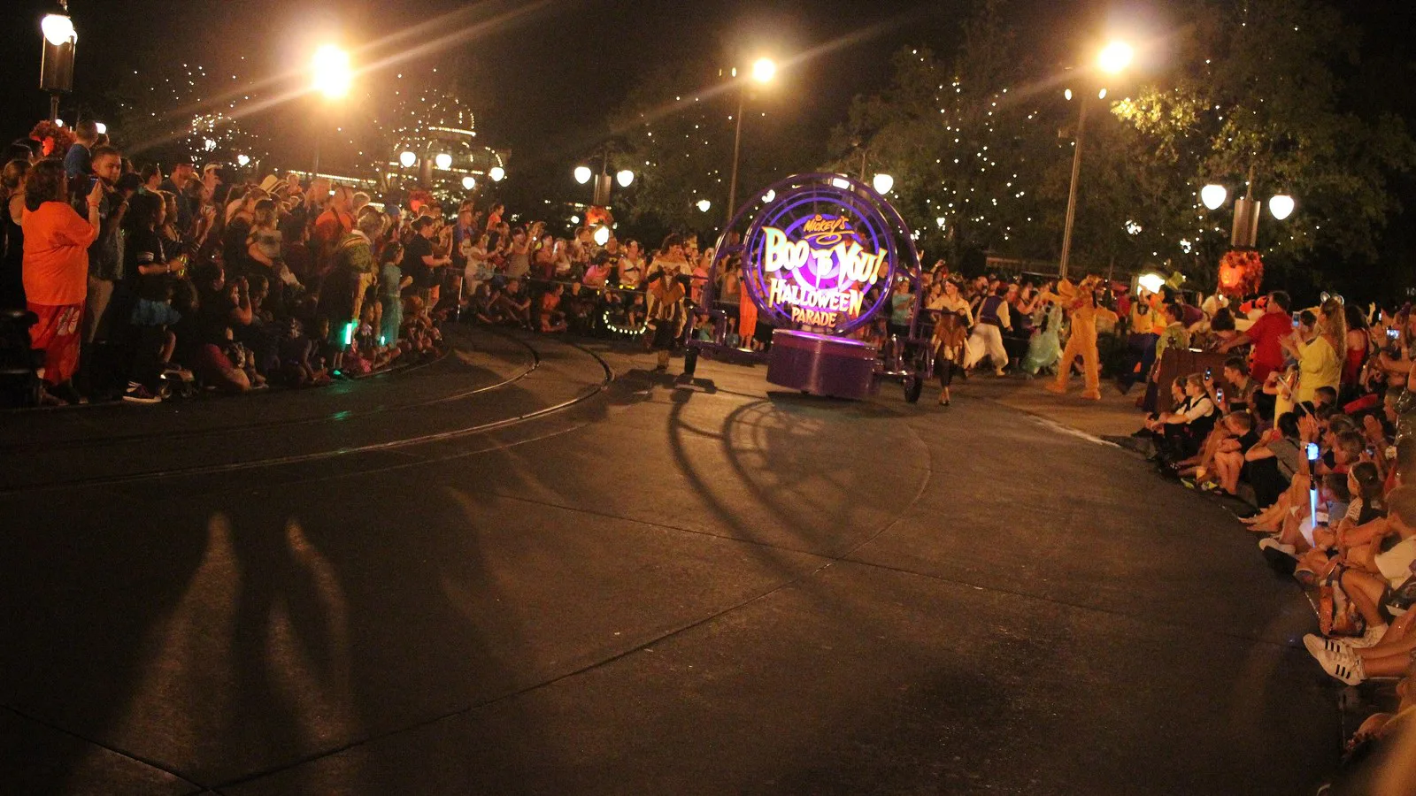 Foto de arquivo do desfile Mickey's Boo-To-You Halloween Parade, à noite, com um carro alegórico iluminado com o logotipo do desfile e o público dos dois lados da rua