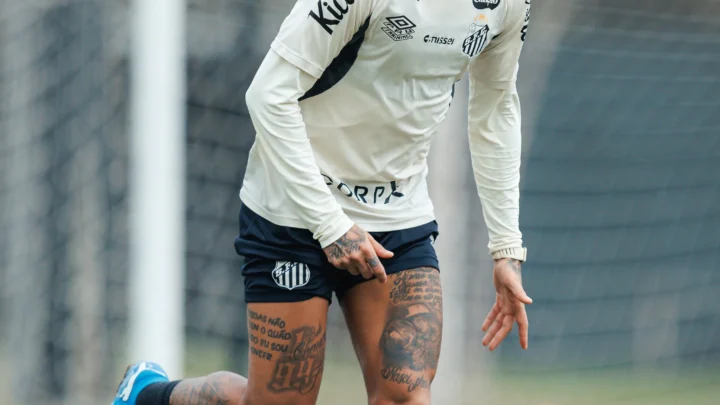 Jogador do Santos em movimento durante treino no Centro de Treinamento Rei Pelé, usando uniforme branco e azul da equipe