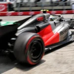 Carro de Fórmula 1 com pintura cinza, vermelha e logotipos da Audi e Revolut acelera em trecho de pista, com desfoque de movimento nas rodas
