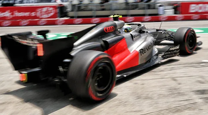 Carro de Fórmula 1 com pintura cinza, vermelha e logotipos da Audi e Revolut acelera em trecho de pista, com desfoque de movimento nas rodas