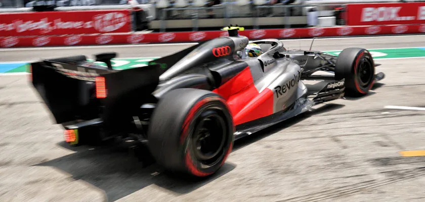 Carro de Fórmula 1 com pintura cinza, vermelha e logotipos da Audi e Revolut acelera em trecho de pista, com desfoque de movimento nas rodas