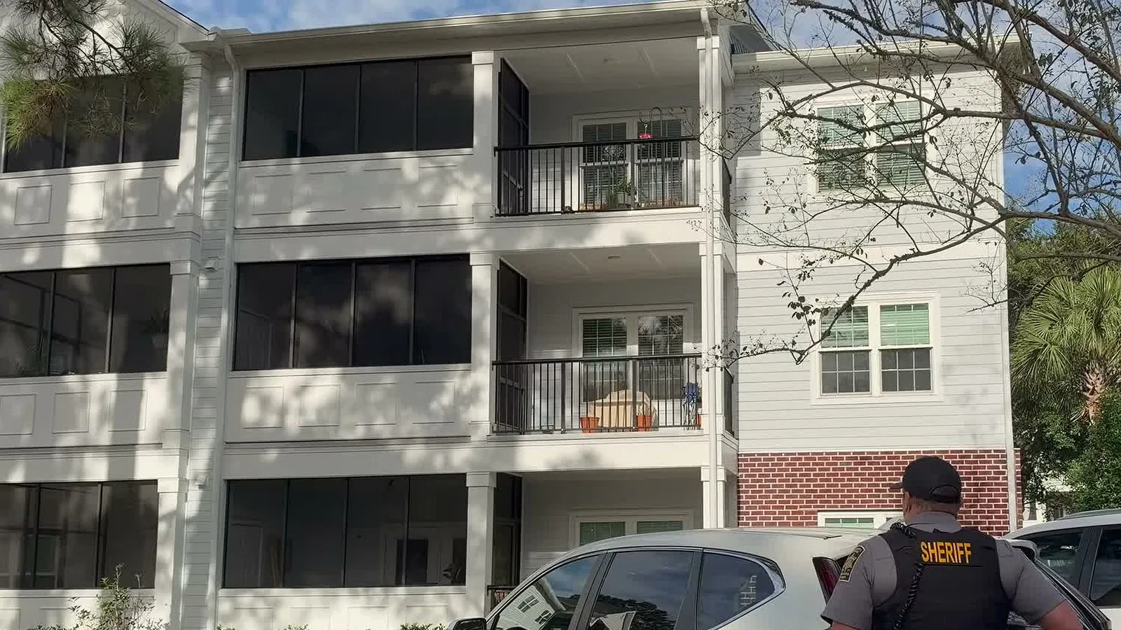 Agente do xerifado diante de um prédio de apartamentos de três andares em James Island, onde o suspeito foi localizado