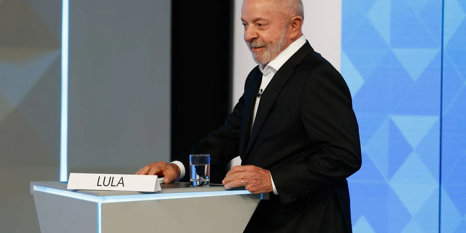 Lula, sorrindo, apoia as mãos no púlpito com a placa "LULA" no estúdio do debate da TV Globo, no Rio de Janeiro, em 23 de outubro de 2026