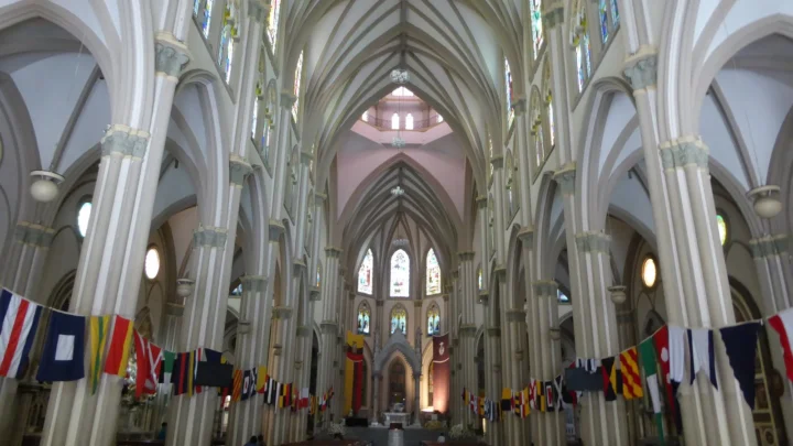 Nave central da Catedral de Guayaquil, em estilo neogótico, com colunas brancas, vitrais e bandeirolas coloridas (foto de arquivo; não é a igreja do Perpétuo Socorro)