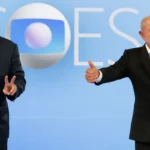 Flávio Bolsonaro, à esquerda, e Lula, à direita, gesticulam para os fotógrafos no cenário do debate da TV Globo, no Rio de Janeiro, em 23 de outubro de 2026