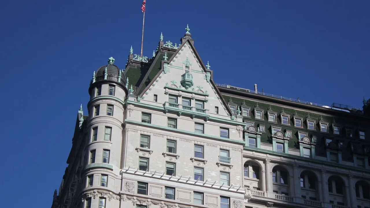 Fachada do Hotel Plaza vista da Quinta Avenida, em Manhattan, com o telhado verde e uma torre arredondada sob céu azul