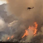 Imagem de arquivo (outubro de 2007, condado de San Diego): helicóptero joga água sobre as chamas de um incêndio florestal numa encosta, sob fumaça densa