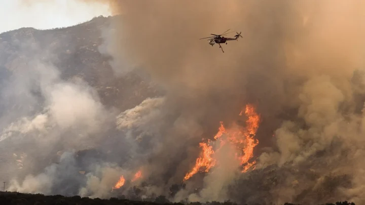 Imagem de arquivo (outubro de 2007, condado de San Diego): helicóptero joga água sobre as chamas de um incêndio florestal numa encosta, sob fumaça densa