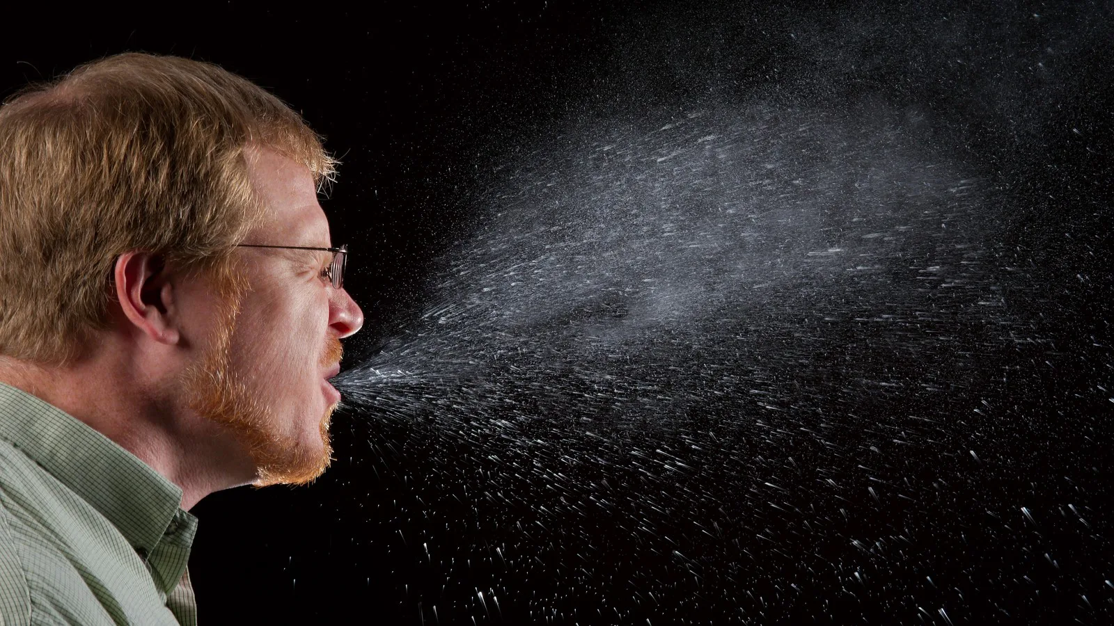 Homem espirra e solta uma nuvem de gotículas de saliva, em foto do CDC que mostra por que é preciso cobrir a boca ao tossir ou espirrar