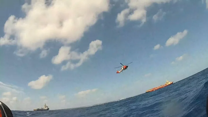 Helicóptero da Guarda Costeira sobre o mar, visto da água, com embarcações no horizonte