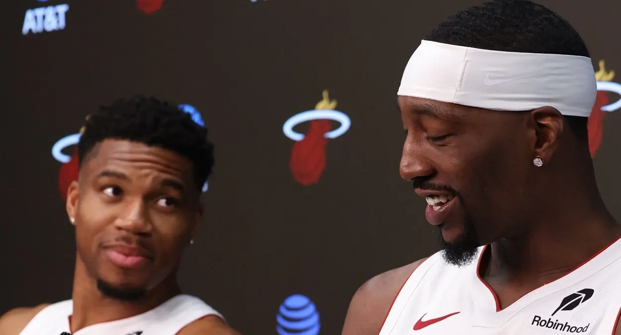 Dois jogadores de camisa branca do Miami Heat sorriem em entrevista coletiva, um deles de faixa branca na cabeça, diante de um painel com o logo da equipe e da AT&T