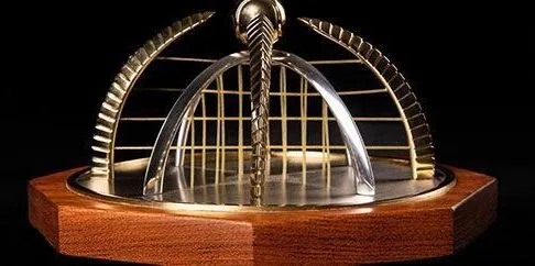 Troféu do SP Open repousa sobre base de madeira, exibindo design em metal dourado com estrutura em forma de cúpula e corrente central