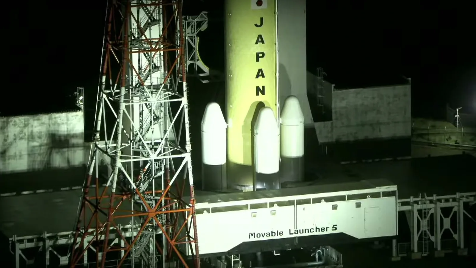 Foguete H3 iluminado na plataforma, com a palavra JAPAN pintada no corpo amarelo, minutos antes da decolagem