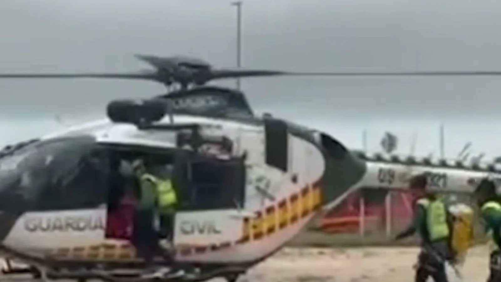 Helicóptero da Guarda Civil pousado em terreno de terra enquanto agentes com coletes amarelos se preparam para embarcar