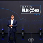 Flávio Bolsonaro e Lula em pé no palco do debate da Band, com o painel "Band Eleições 2026" ao fundo
