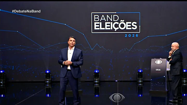 Flávio Bolsonaro e Lula em pé no palco do debate da Band, com o painel "Band Eleições 2026" ao fundo