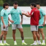 Jogadores do Palmeiras conversam durante treinamento em campo, com um integrante da comissão técnica orientando o grupo
