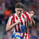 Jogador de camisa listrada vermelha e branca, com escudo do clube e patrocínio da Riyadh Air, chuta a bola durante partida em estádio lotado