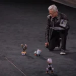 Jensen Huang, CEO da Nvidia, ajoelhado no palco com um notebook na mão enquanto um dos robôs-pato Microduck fica de cabeça para baixo ao dar uma cambalhota, na keynote da GTC Berlim, em 21 de outubro de 2026