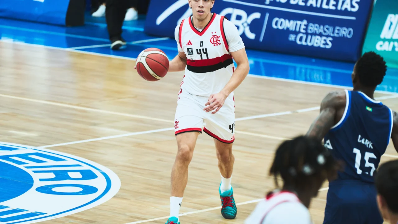 Jogador do Flamengo, de camisa branca e número 44, conduz a bola em quadra durante partida de basquete, com um adversário de uniforme azul-marinho em primeiro plano