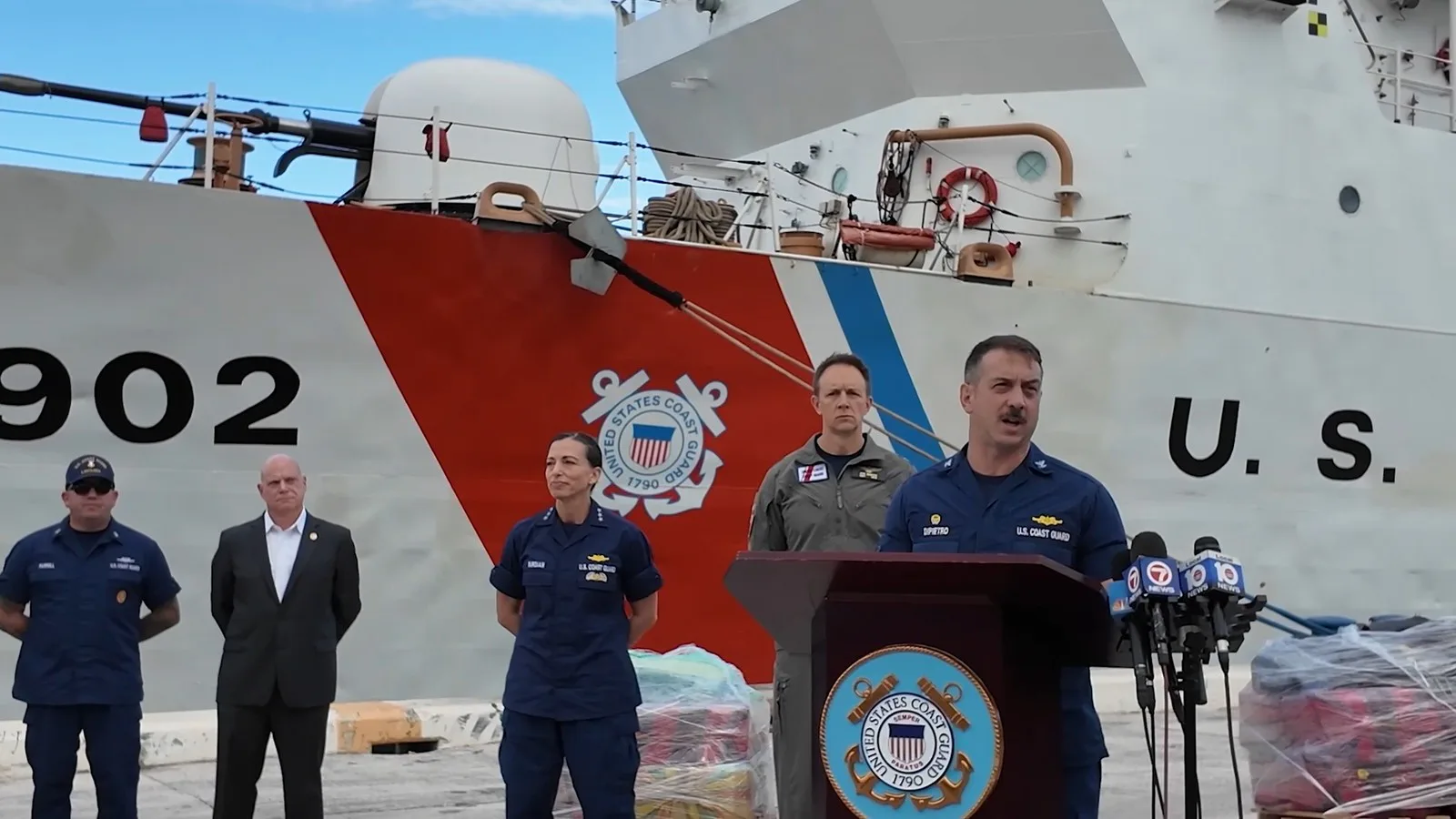 Oficial da Guarda Costeira fala à imprensa no cais, diante do casco 902 do navio Tampa, com autoridades ao lado